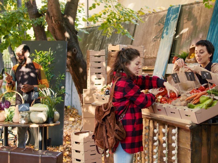 Puesto de mercado al aire libre con cajas de producto y clientes eligiendo